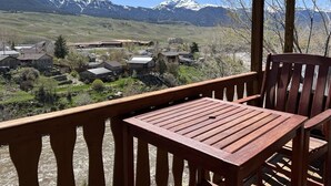 A wooden deck with a table and chairs overlooking a village with mountains in the background. - Cozy Eagles Nest Cabin Above the River! 6 Blocks from Yellowstone Park  (Gardiner)