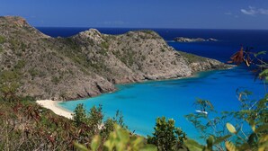 Un paisaje costero con mar azul cristalino, acantilados rocosos y una playa arenosa.