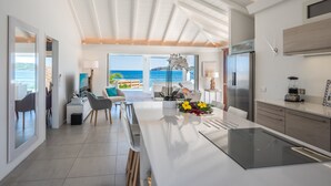 Una cocina moderna con una isla grande, un comedor con sillas y vista al océano.