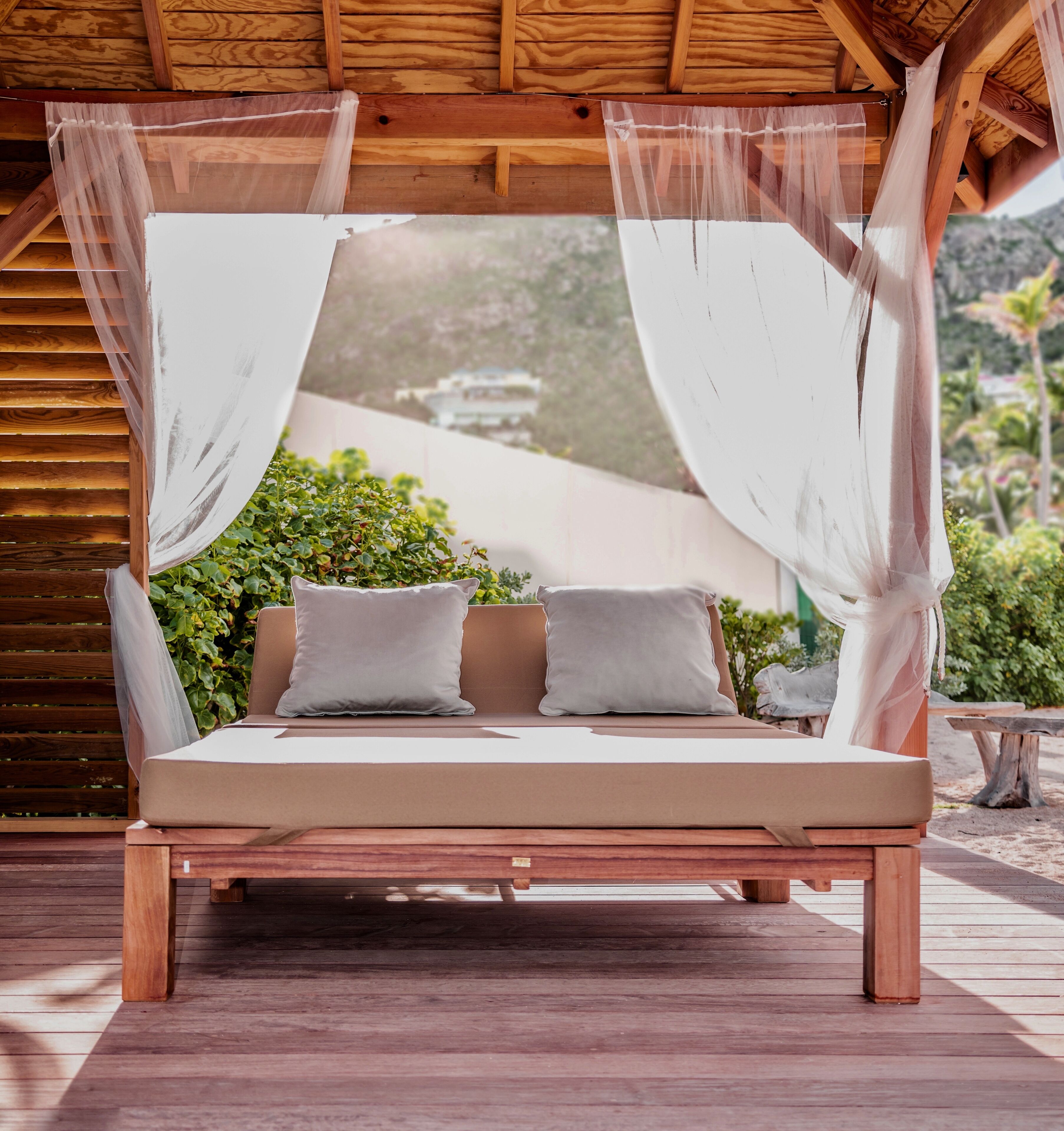 Una cama de madera con dosel, dos almohadas y vista a zonas verdes y edificios al fondo.