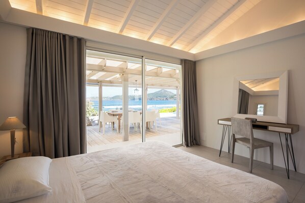 A modern hotel room with a large bed, a desk, and a view of the ocean.