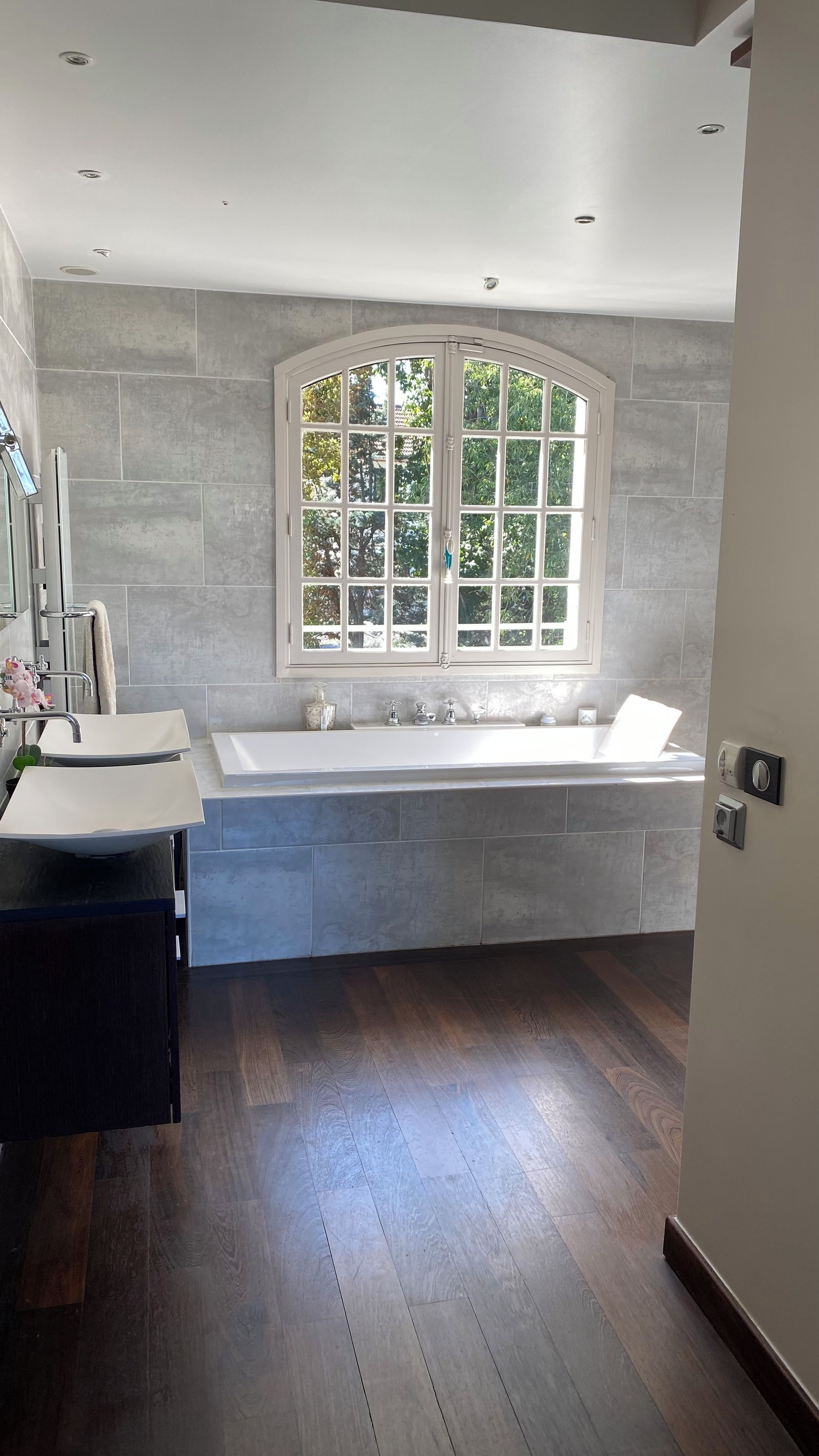 A modern bathroom with a freestanding bathtub, a large window with a view of trees, and a vanity with a mirror.