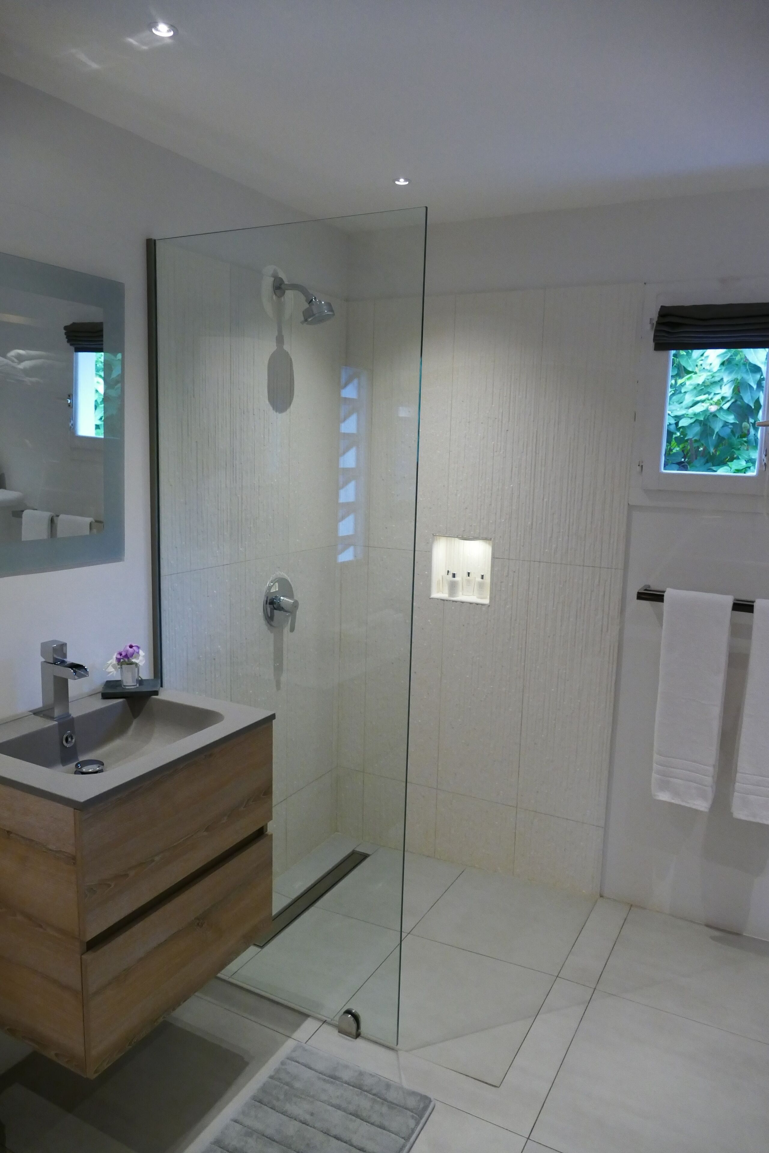 Une salle de bain moderne avec une douche à parois de verre, un meuble-lavabo en bois et un grand miroir.