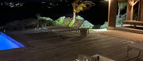A wooden deck with a pool, lounge chairs, and a table set for dining.