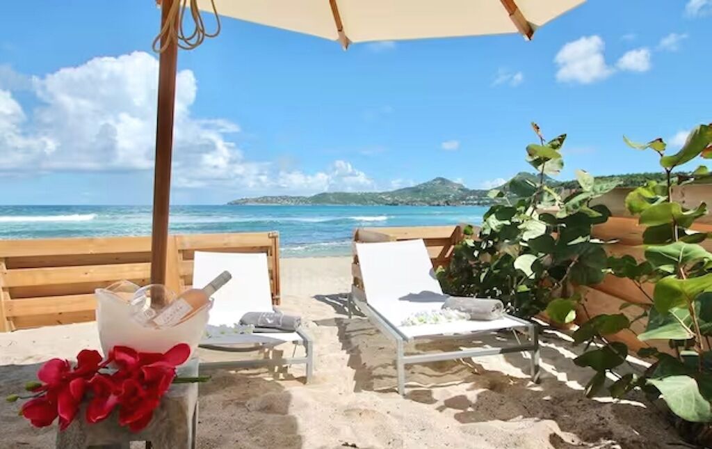 A beachside lounge with two lounge chairs, a bottle of champagne, and a bouquet of flowers.