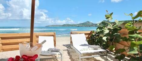 A beachside lounge with two lounge chairs, a bottle of champagne, and a bouquet of flowers.