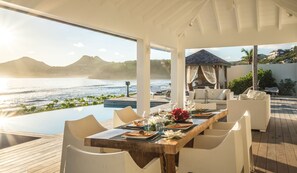 A covered outdoor dining area with a view of the sea and mountains.