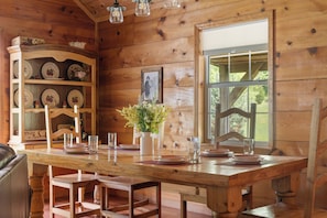 A wooden dining room with a large table, chairs, a cabinet with dishes, and a window.
