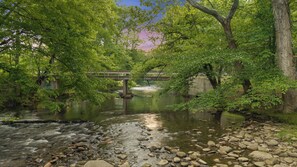 A river with rocks and a bridge in a wooded area. - STUNNING CABIN, TROUT STREAM, HUGE GAMEROOM, HOT TUB,FIRE PIT,TUBING,& MEMORIES! (Cosby)