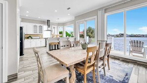 A spacious kitchen with white cabinets, a wooden dining table, and large windows overlooking a body of water. - Bella Vita | September Deals and Peaceful Beaches!! | Tennis Court Access!! | 1PM Check In! | Lakefront Patio with Grilling Station, Private Pool & new Polywood Furniture | Incredible Views! Steps from The Crab Trap | Game Room! (Destin)