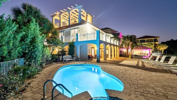 A large house with a swimming pool, surrounded by palm trees and a well-lit patio area. - Bella Vita | September Deals and Peaceful Beaches!! | Tennis Court Access!! | 1PM Check In! | Lakefront Patio with Grilling Station, Private Pool & new Polywood Furniture | Incredible Views! Steps from The Crab Trap | Game Room! (Destin)