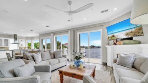 A spacious living area with a large flat-screen TV, a ceiling fan, and a balcony with a view of the ocean. - Bella Vita | September Deals and Peaceful Beaches!! | Tennis Court Access!! | 1PM Check In! | Lakefront Patio with Grilling Station, Private Pool & new Polywood Furniture | Incredible Views! Steps from The Crab Trap | Game Room! (Destin)