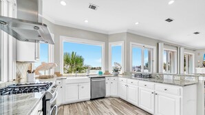 A modern kitchen with white cabinets, a stainless steel range hood, and a large window offering a view of palm trees. - Bella Vita | September Deals and Peaceful Beaches!! | Tennis Court Access!! | 1PM Check In! | Lakefront Patio with Grilling Station, Private Pool & new Polywood Furniture | Incredible Views! Steps from The Crab Trap | Game Room! (Destin)