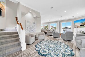A spacious living area with a staircase, multiple seating options, and a large window offering a view.
