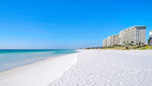 A beach with white sand, clear blue water, and a row of multi-story buildings in the background. - Bella Vita | September Deals and Peaceful Beaches!! | Tennis Court Access!! | 1PM Check In! | Lakefront Patio with Grilling Station, Private Pool & new Polywood Furniture | Incredible Views! Steps from The Crab Trap | Game Room! (Destin)