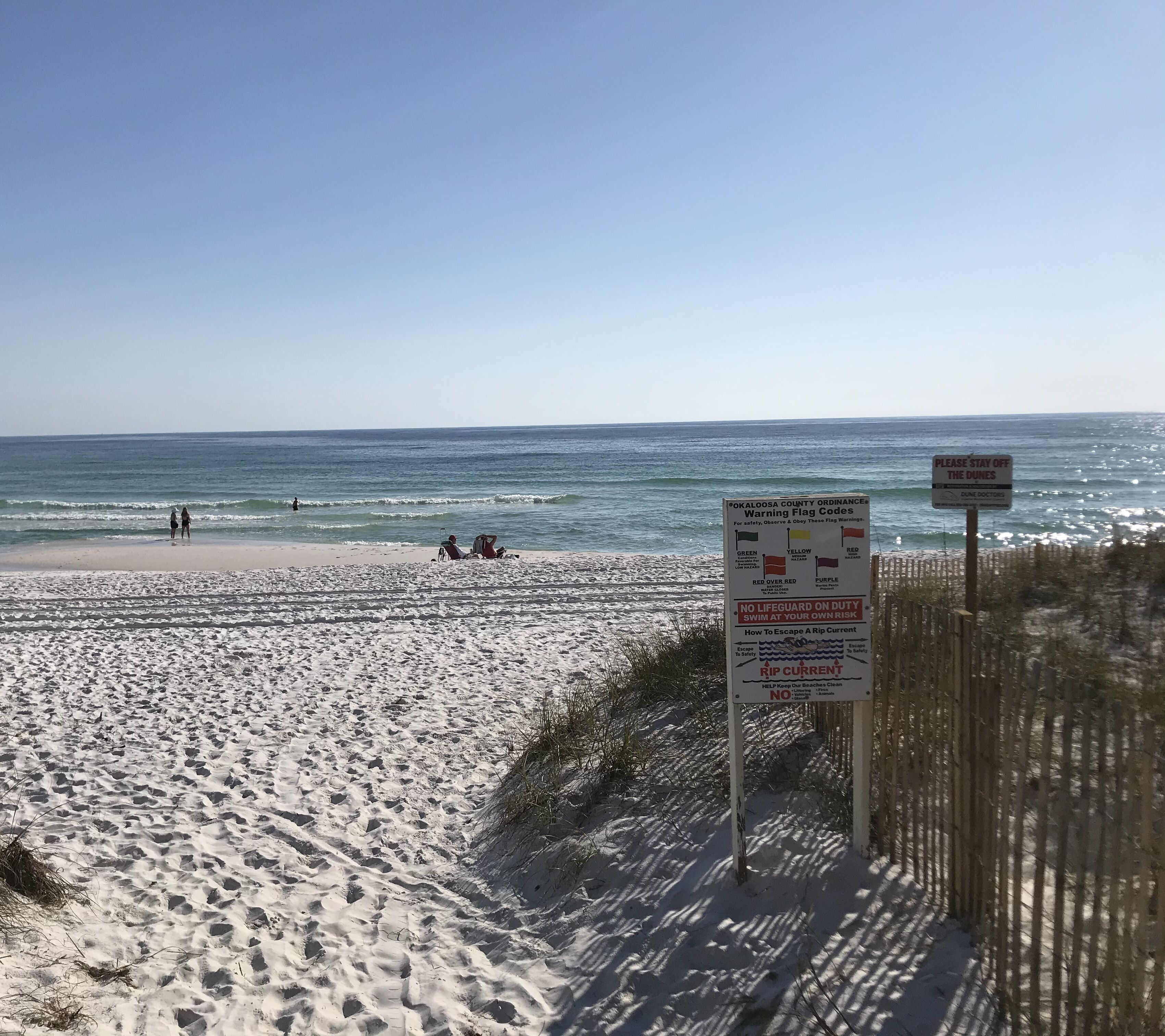 Une plage avec un panneau d’avertissement concernant la sécurité des dunes et une clôture.