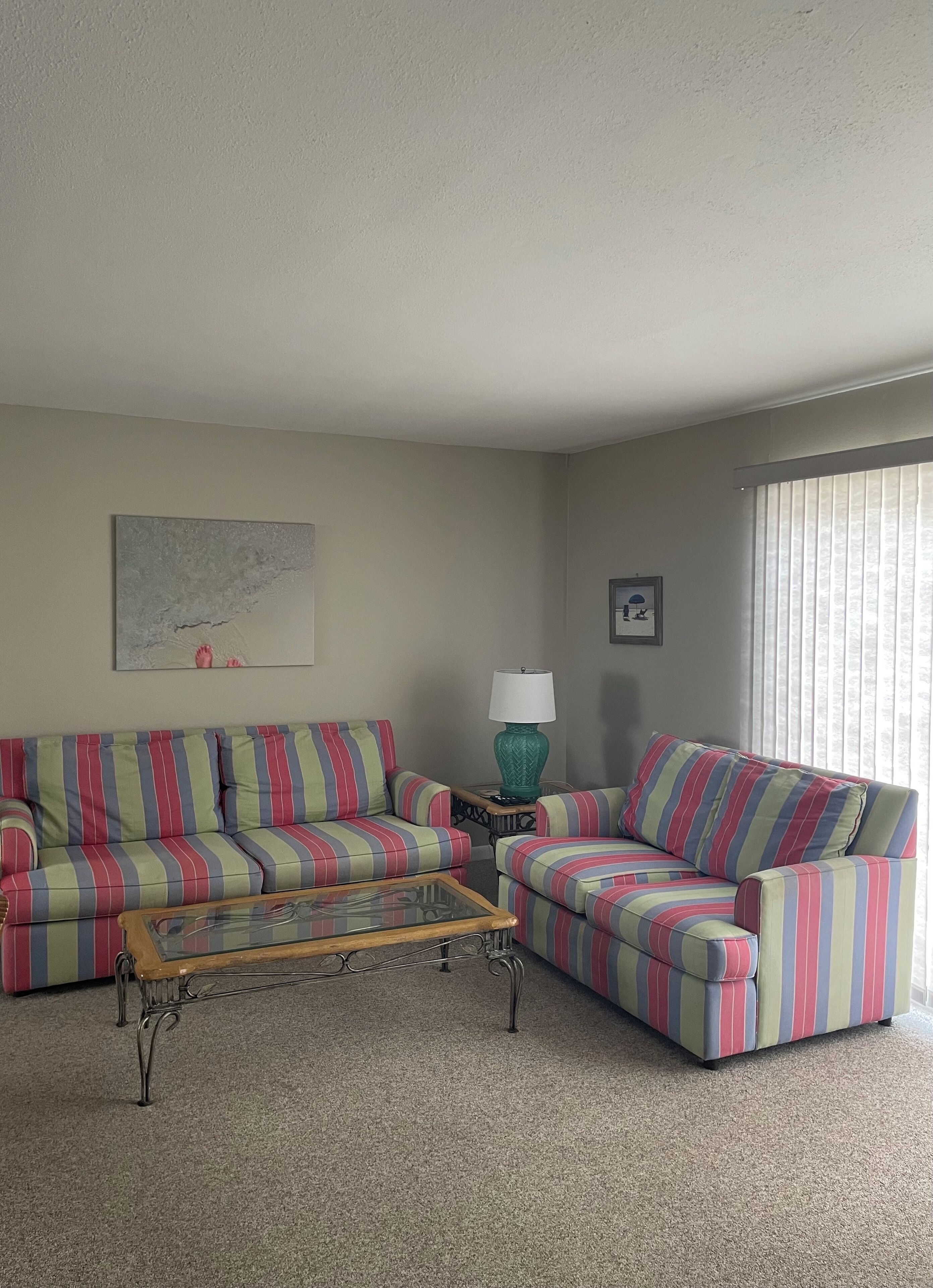 A living room with striped sofas, a glass coffee table, a teal lamp, and a framed picture on the wall.