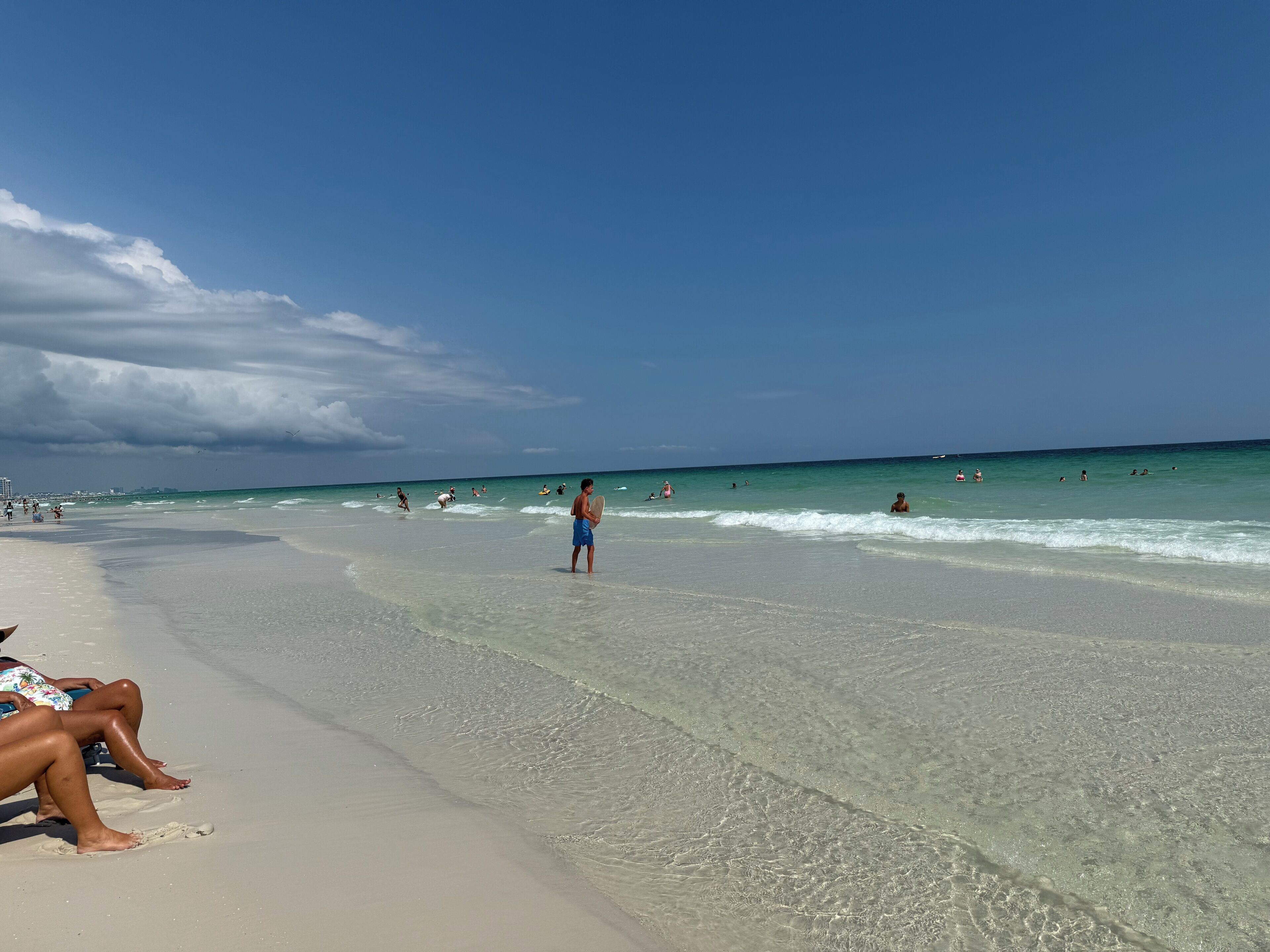 A beach with clear water, people swimming and walking along the shore.