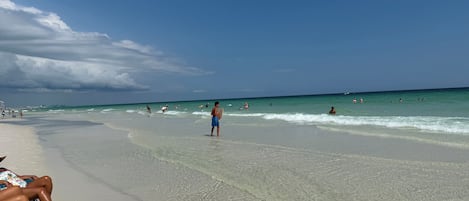 A beach with clear water, people swimming and walking along the shore.