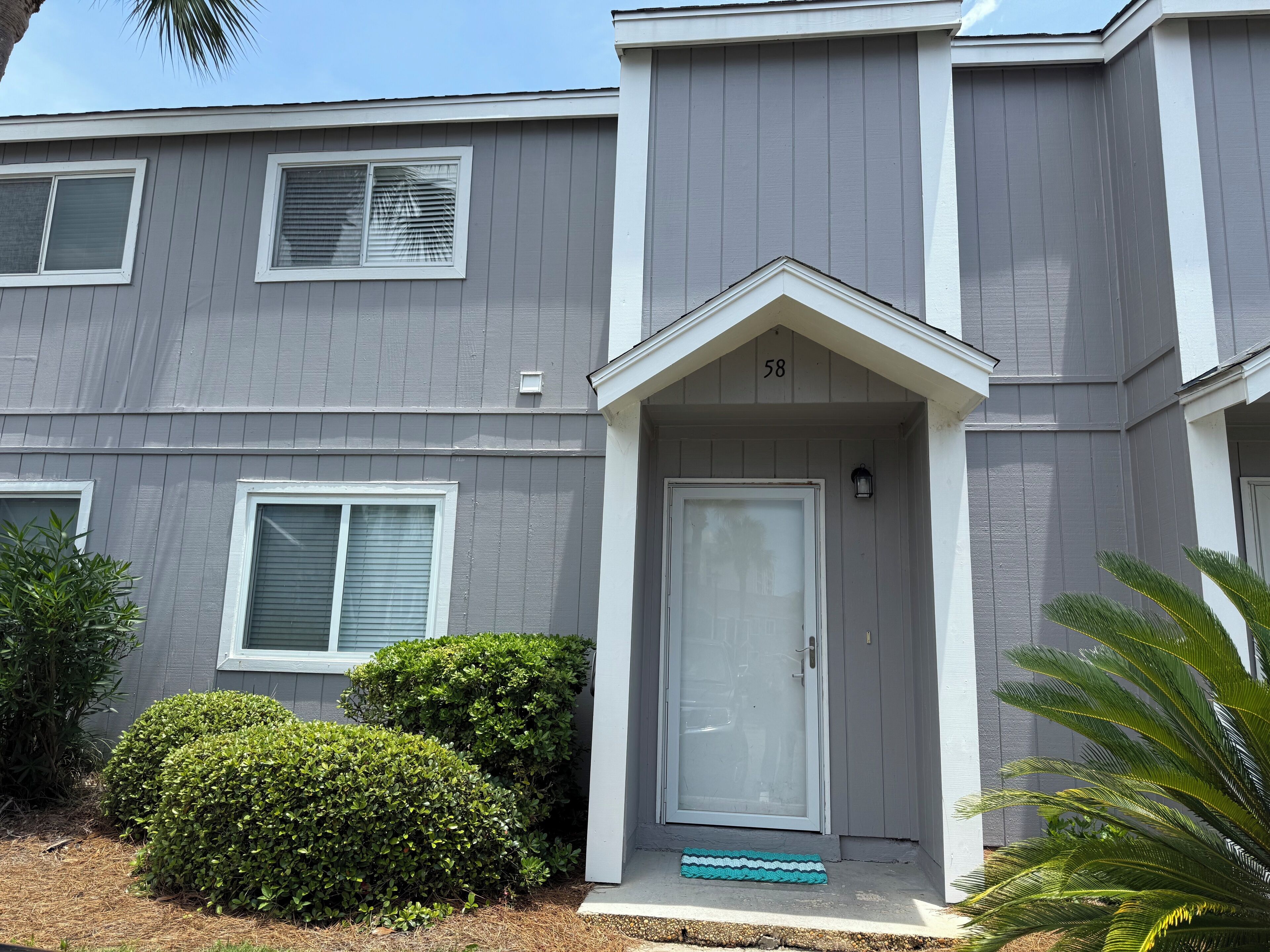 A two-story residential building with a grey exterior, white trim, and a number '58' above the front door.