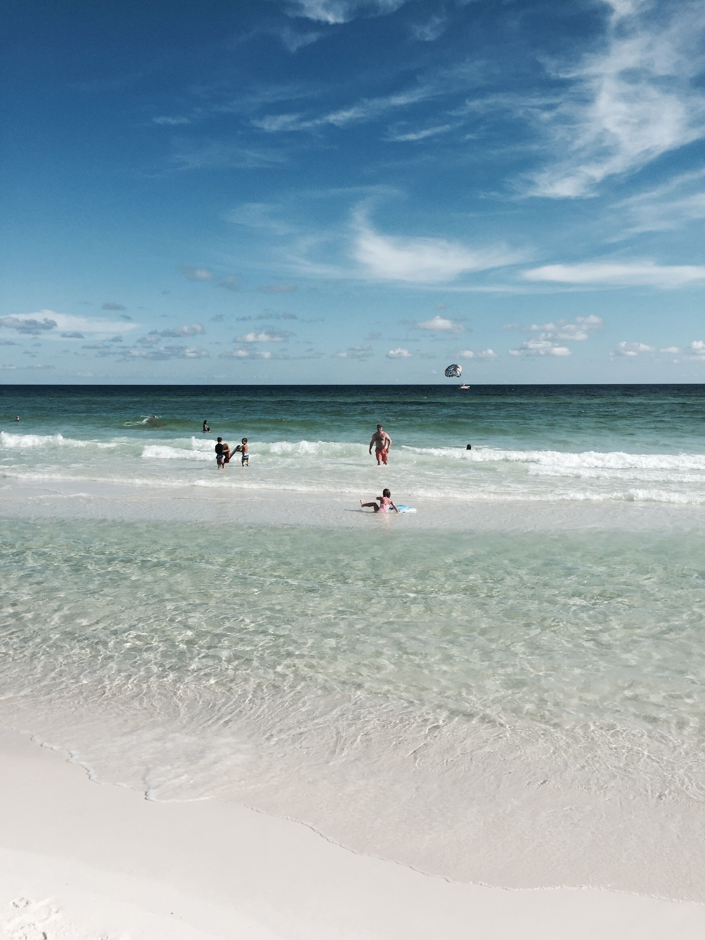 A beach with clear water, a few people, and a boat in the distance.