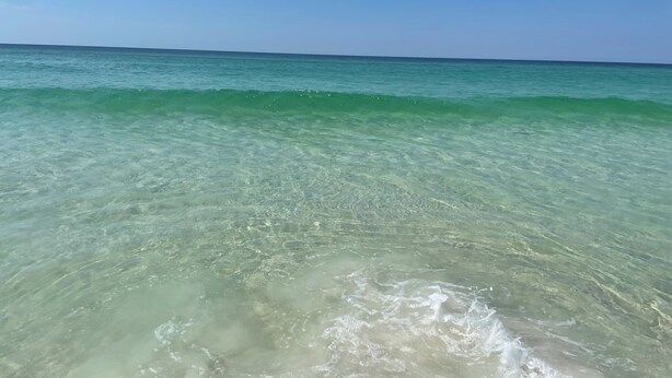 A clear view of a beach with gentle waves and a calm sea under a clear sky. - 4 Min Walk to Beach and Lakefront Patio! Patio + Community Pool! (Destin)