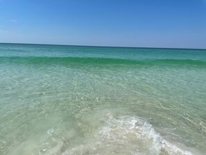Visão nítida de uma praia com ondas suaves e um mar calmo sob um céu limpo.