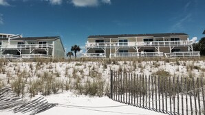 A beachfront hotel with multiple balconies, a sandy beach in the foreground, and a clear blue sky. - 4 Min Walk to Beach and Lakefront Patio! Patio + Community Pool! (Destin)