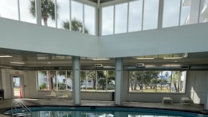 An indoor swimming pool with clear glass walls, a pool ladder, and lounge chairs.
