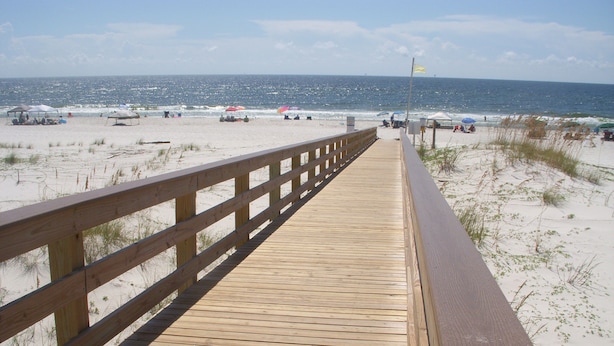 A wooden boardwalk leading to a beach with umbrellas and people.