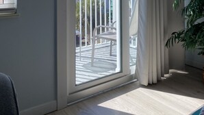 A room with a sliding glass door leading to a balcony with a white railing, a potted plant, and a notebook on the floor.