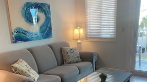 A living room with a grey sofa, a glass coffee table, and a painting on the wall.