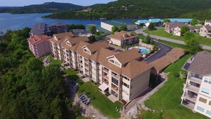 Un hôtel à plusieurs étages doté d’une piscine, situé près d’un lac, avec des bateaux et des maisons en arrière-plan.