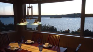 Une table à manger dressée pour quatre personnes, avec vue sur un lac et des collines en arrière-plan.