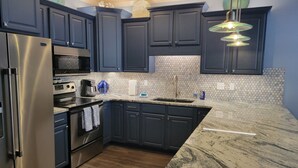 Une cuisine moderne avec des meubles de couleur sombre, des appareils électroménagers en acier inoxydable et un plan de travail en marbre.