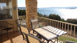 Un balcon avec une table et des chaises, donnant sur une étendue d’eau et sur une terre lointaine.
