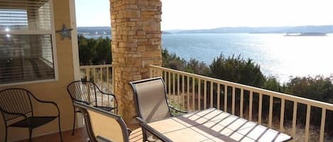 A balcony with a table and chairs, overlooking a body of water and distant land.