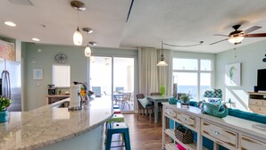 A modern kitchen with a central island, bar stools, and a dining area with a view. - Delicious 3BR-3BA Direct Gulf Front Condo (Panama City Beach)