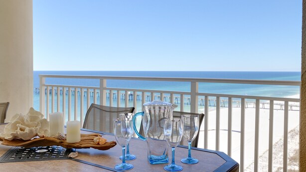 A table with a tray of decorative items and glasses, overlooking a beach with a white railing and clear blue sky. - Delicious 3BR-3BA Direct Gulf Front Condo (Panama City Beach)
