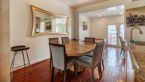 Un coin repas avec une table et des chaises en bois, un grand miroir au mur et un tableau au-dessus de la porte.