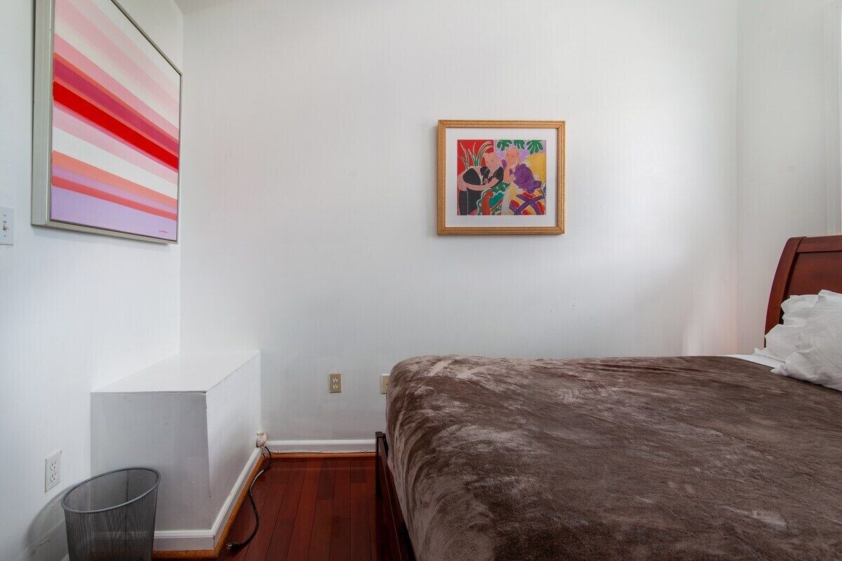 Une chambre à coucher avec un lit, une œuvre d’art encadrée au mur et une poubelle.