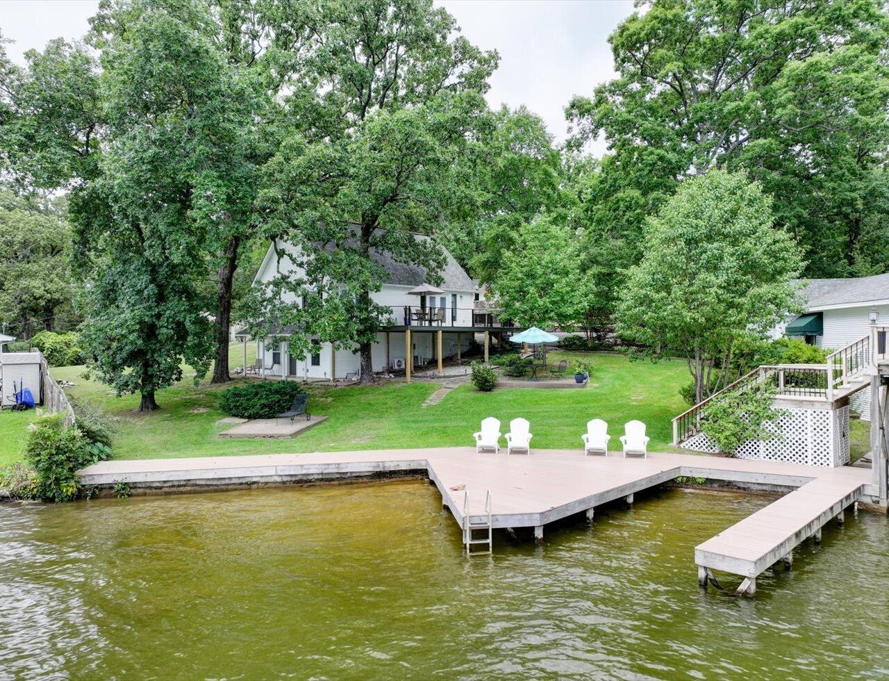A lakeside property with a dock, outdoor seating, and a house with a deck.