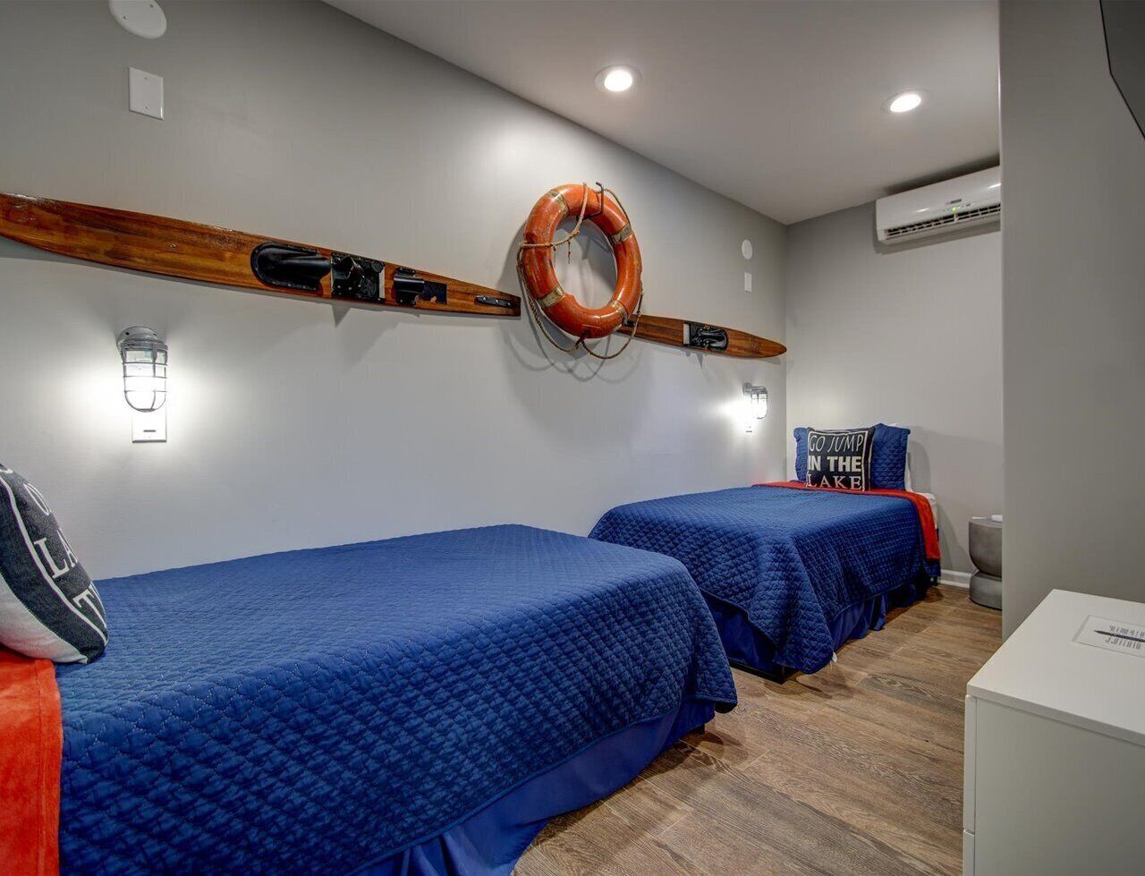 Ein Zimmer mit zwei Betten, einem Rettungsring an der Wand und einem Schild mit der Aufschrift 'GO JUMP IN THE LAKE'.