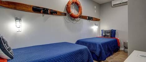 Ein Zimmer mit zwei Betten, einem Rettungsring an der Wand und einem Schild mit der Aufschrift 'GO JUMP IN THE LAKE'.
