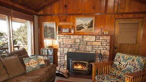 A cozy living room with a fireplace, wooden furniture, and framed artwork on the walls.