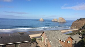 A coastal view with two prominent rock formations in the sea, a sandy beach, and residential buildings with sloped roofs.