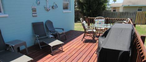 A wooden deck with outdoor furniture, a grill, and a potted plant.