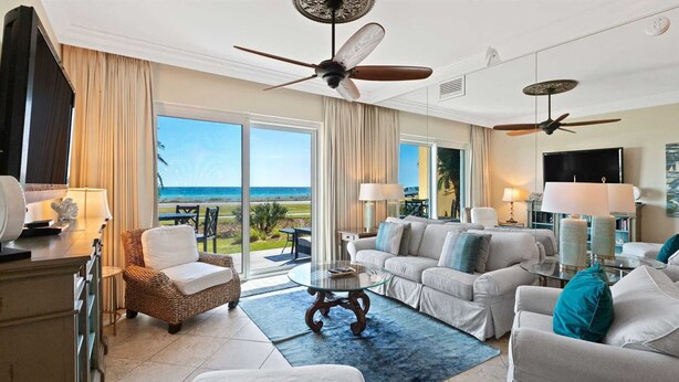 Un salón amplio con un gran ventanal con vistas a la playa, amueblado con un sofá, sillones y una mesa de centro.