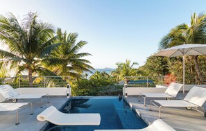 A pool area with lounge chairs and umbrellas, surrounded by palm trees and a view of the ocean. - ST BART LUXURY VILLA SKRUTTEN,  WITH OCEAN VIEW AND CONTEMPORARY FURNISHING (Pointe Milou)