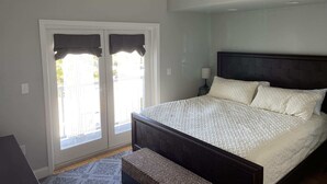 Ein Schlafzimmer mit Bett, Deckenventilator, Nachttisch, Lampe und Blick durch die Tür.